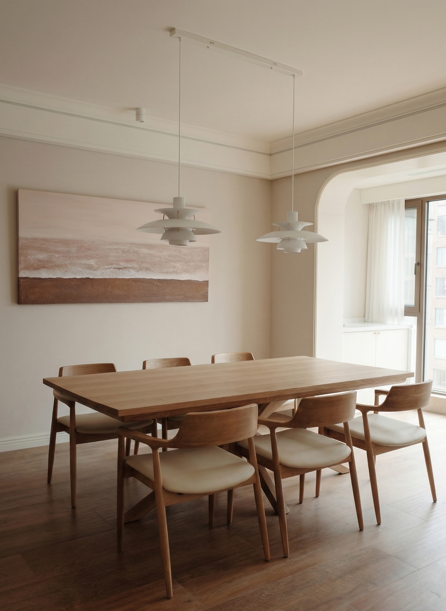 Dining room with a light oak table, six chairs with cream cushions, two white pendant lights and an abstract painting