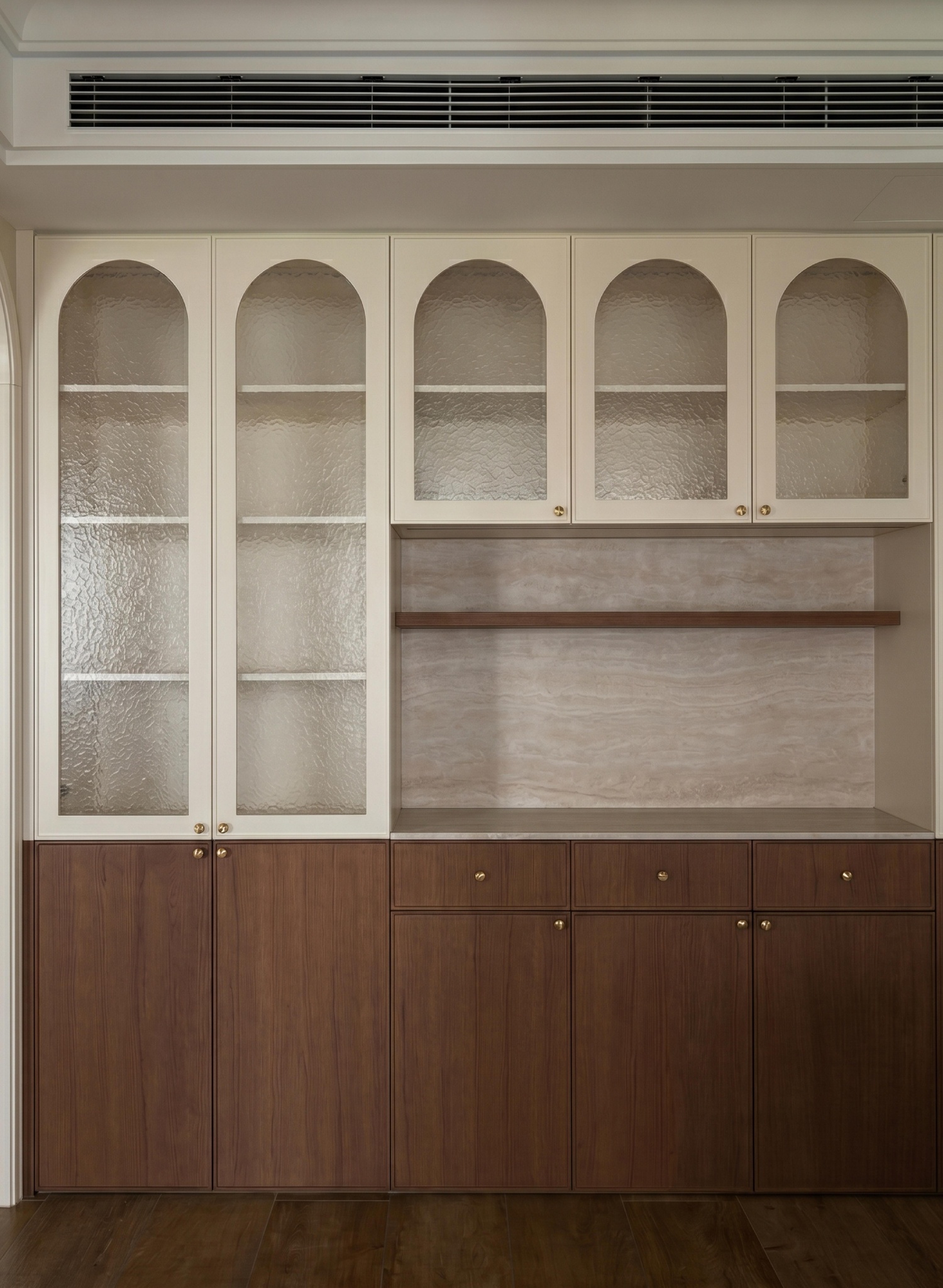 Built-in cabinet with arched glass doors, warm wood lower section and brass knobs