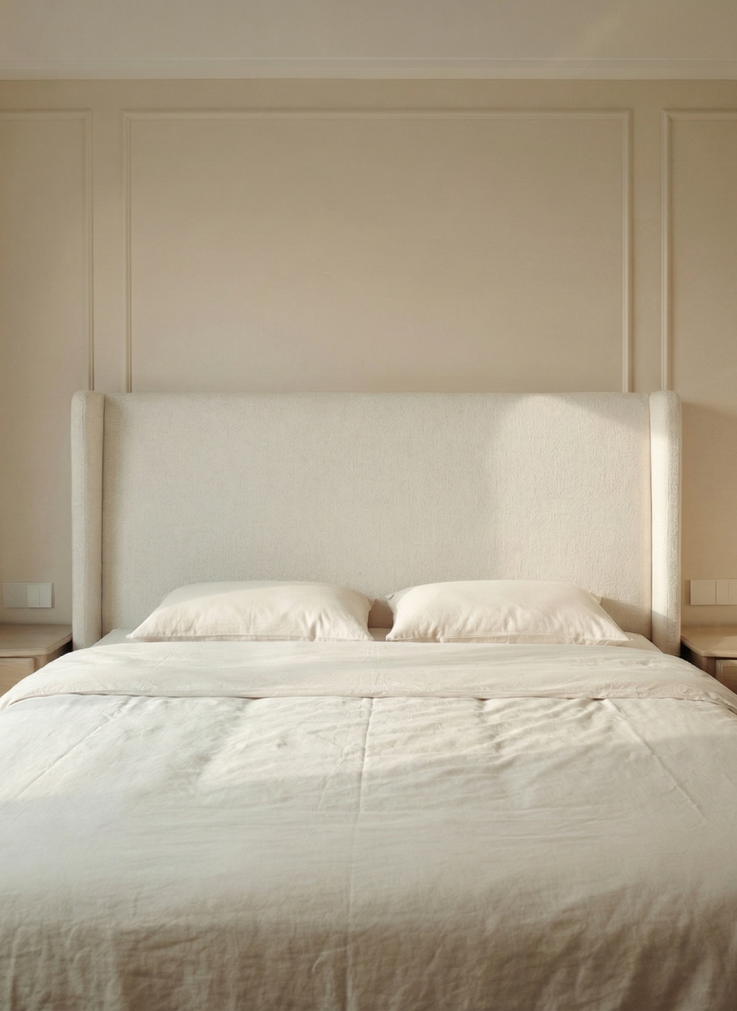 Main bedroom with a tall cream headboard, white linens and wall moulding