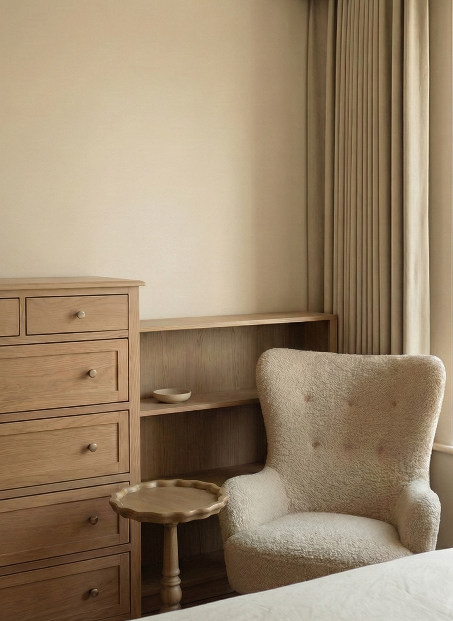 Bedroom corner with a wooden dresser, low bookshelf, scalloped side table and a cream armchair