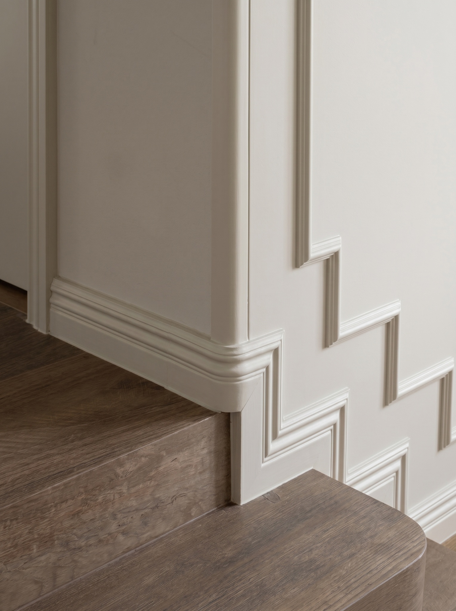 Detail of the wooden staircase meeting the wall, with stepped moulding following the stair profile