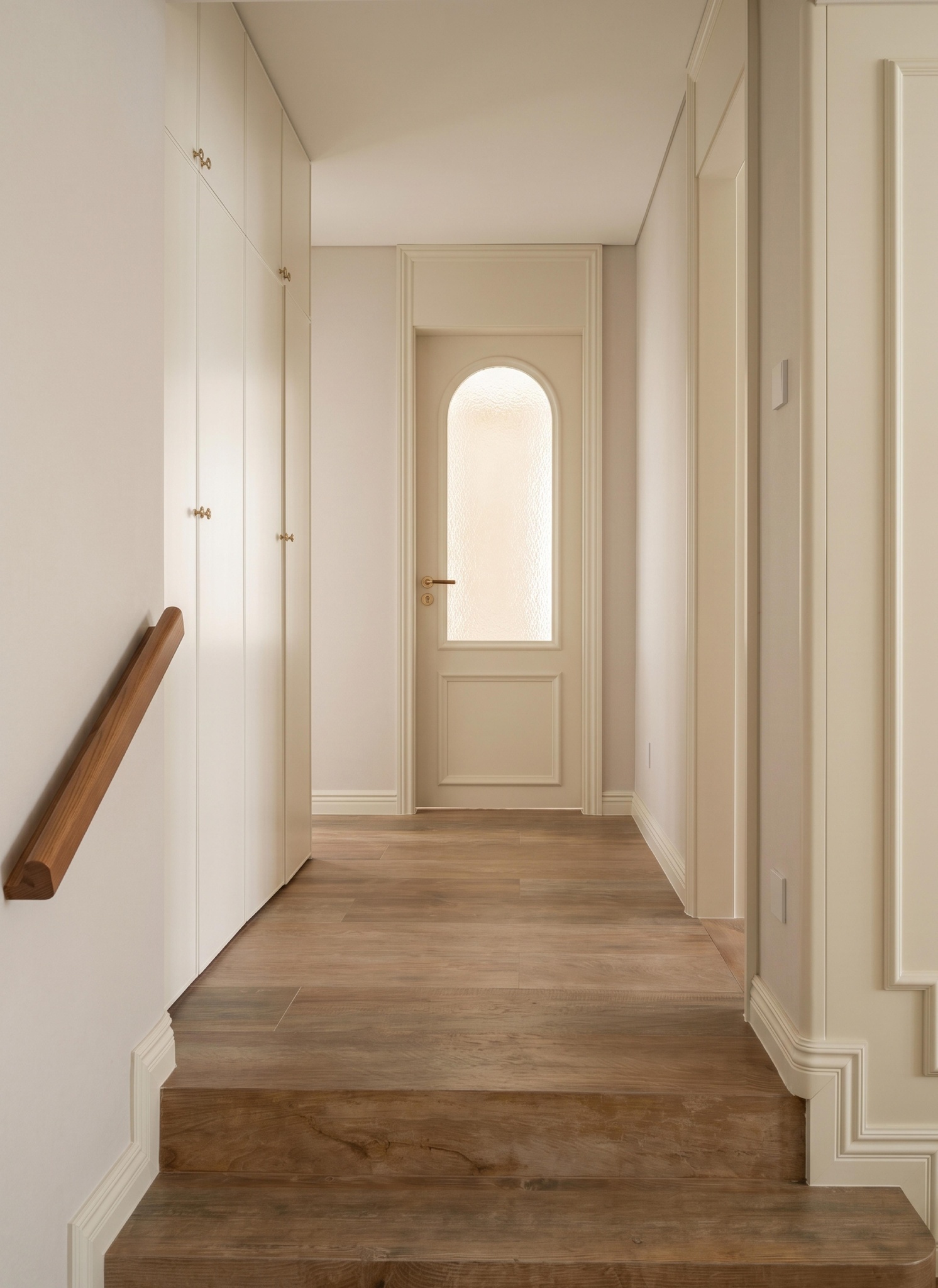Corridor with an arched frosted-glass door, wooden stairs and a dark wood handrail