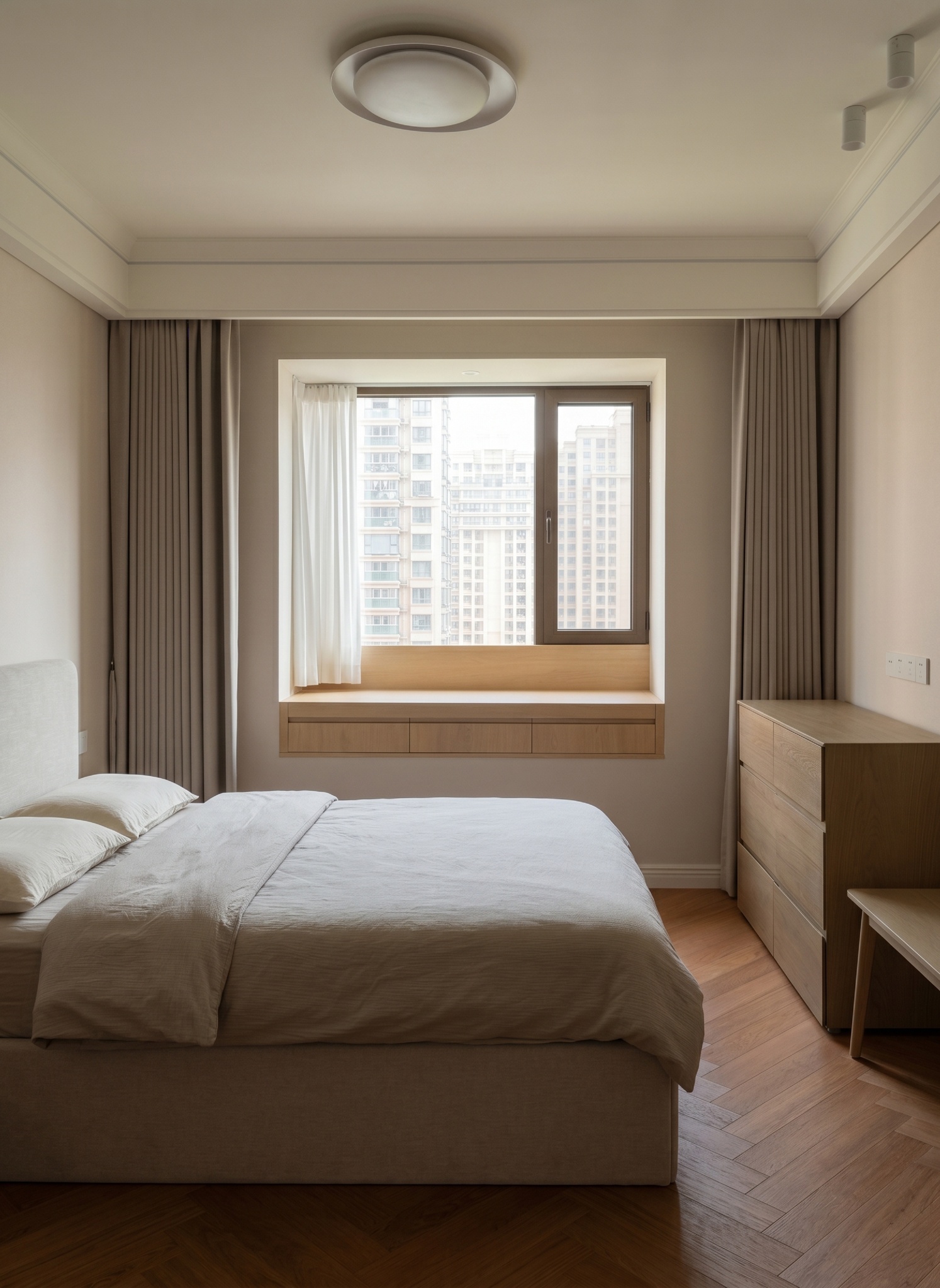 Guest bedroom with a bed, a large window onto the city, a wooden dresser and herringbone floor